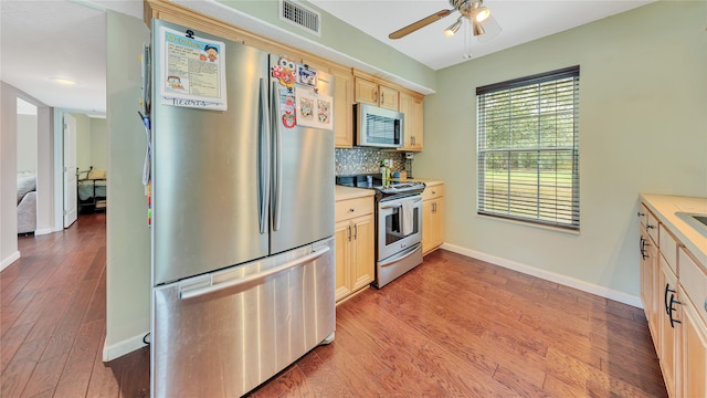 kitchen featuring ceiling fan, stainless steel appliances, decorative backsplash, light brown cabinetry, and light wood-type flooring