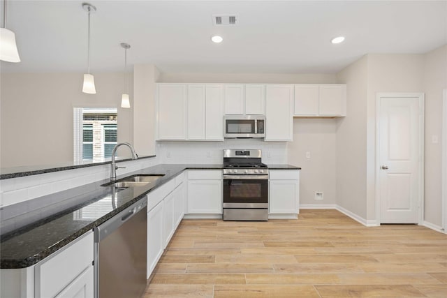 kitchen with pendant lighting, sink, appliances with stainless steel finishes, white cabinets, and dark stone counters