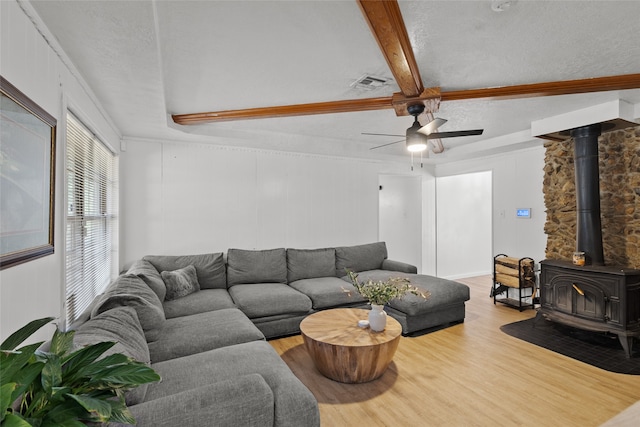 living room featuring hardwood / wood-style flooring, beamed ceiling, a wood stove, a textured ceiling, and ceiling fan