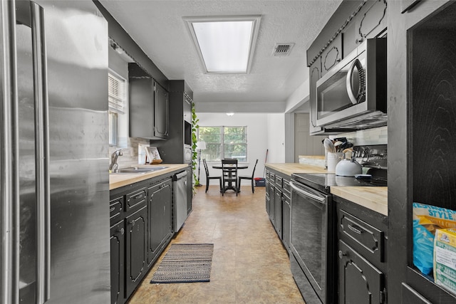 kitchen with wooden counters, stainless steel appliances, backsplash, sink, and a textured ceiling