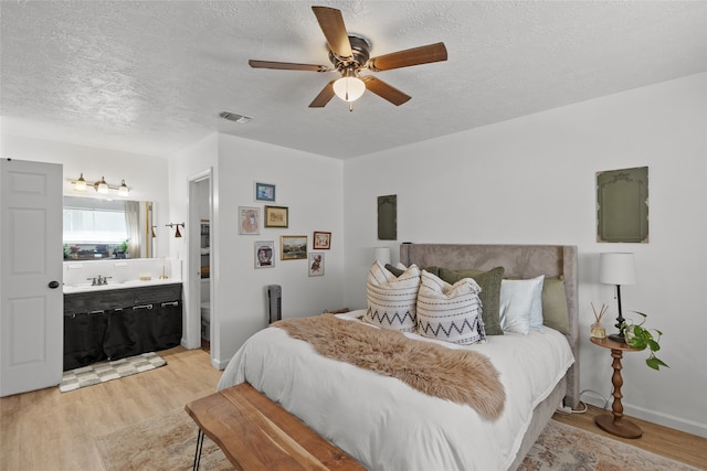 bedroom featuring ceiling fan, a textured ceiling, light wood-type flooring, ensuite bathroom, and sink