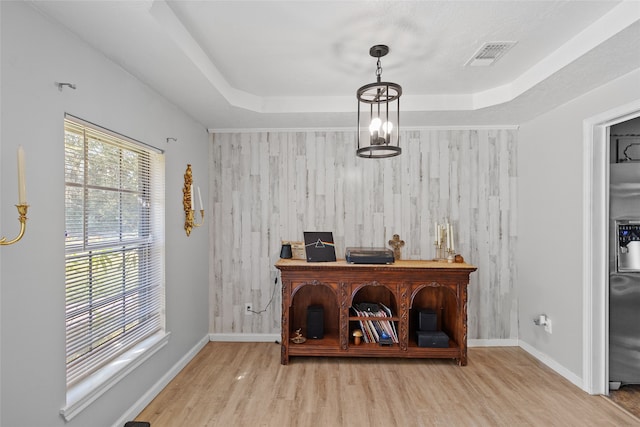 interior space with wooden walls, a tray ceiling, and light hardwood / wood-style floors