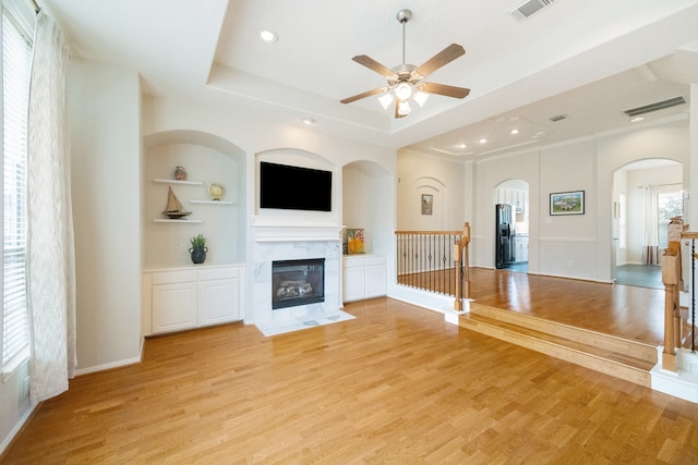 unfurnished living room with built in features, ceiling fan, light hardwood / wood-style floors, and a raised ceiling