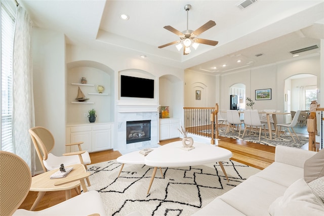 living room featuring ceiling fan, a raised ceiling, light wood-type flooring, and built in shelves