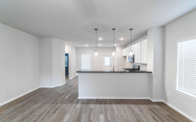 kitchen featuring hardwood / wood-style floors, white cabinets, hanging light fixtures, appliances with stainless steel finishes, and kitchen peninsula