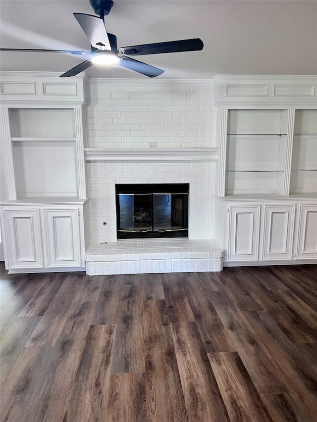 unfurnished living room featuring a brick fireplace, built in shelves, and dark hardwood / wood-style flooring