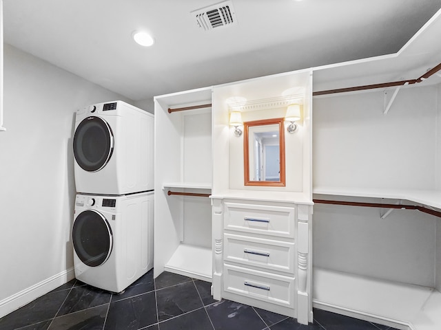 laundry area with stacked washer and dryer and dark tile patterned flooring