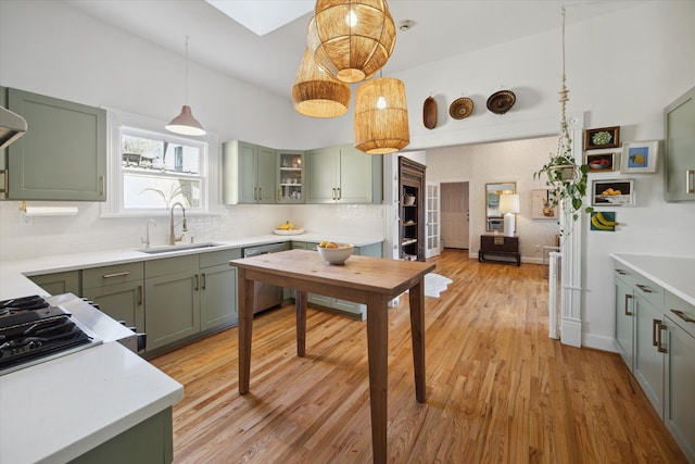 kitchen with hanging light fixtures, stainless steel dishwasher, light hardwood / wood-style flooring, sink, and green cabinetry