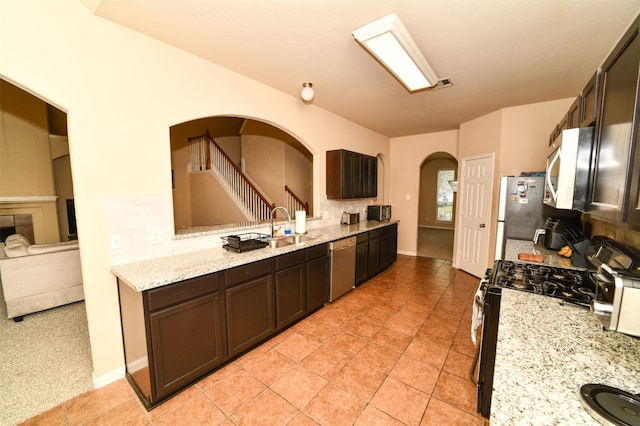 kitchen featuring dark brown cabinets, sink, light stone countertops, light tile patterned floors, and appliances with stainless steel finishes