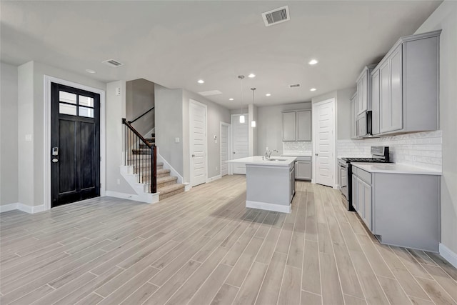 kitchen with gray cabinets, a kitchen island with sink, hanging light fixtures, tasteful backsplash, and stainless steel gas range oven