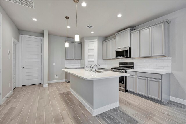 kitchen with gray cabinetry, backsplash, stainless steel appliances, and light wood-type flooring