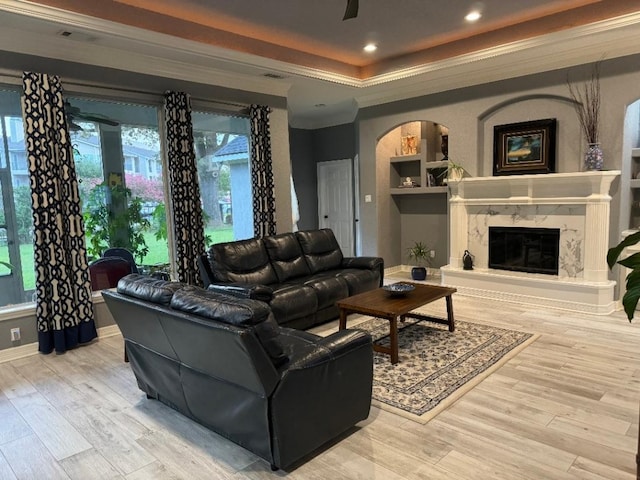 living room featuring a premium fireplace, crown molding, light hardwood / wood-style floors, and a raised ceiling