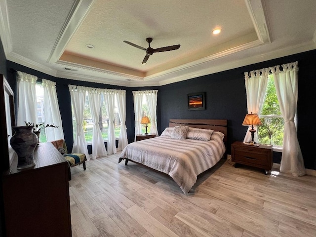 bedroom with light hardwood / wood-style flooring, multiple windows, a tray ceiling, and ceiling fan