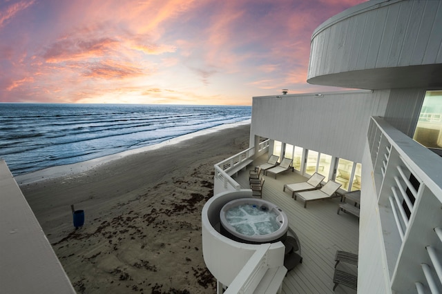 balcony at dusk featuring a water view and a view of the beach