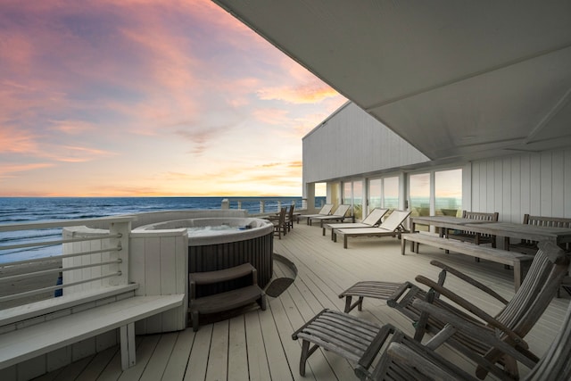 deck at dusk with a water view, a hot tub, and a view of the beach