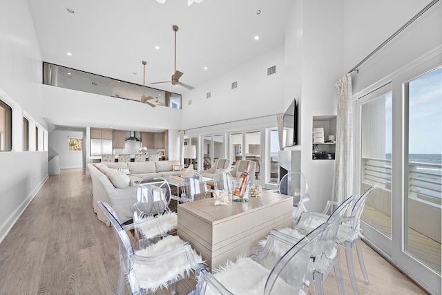 living room with a wealth of natural light, a towering ceiling, light hardwood / wood-style floors, and ceiling fan