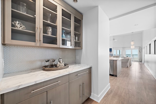 bar featuring backsplash, light stone counters, light hardwood / wood-style floors, and stainless steel dishwasher