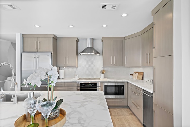 kitchen featuring wall chimney exhaust hood, light hardwood / wood-style floors, backsplash, and appliances with stainless steel finishes