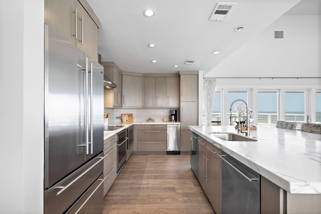 kitchen featuring a water view, sink, an island with sink, appliances with stainless steel finishes, and dark hardwood / wood-style flooring