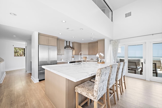 kitchen featuring a healthy amount of sunlight, stainless steel built in fridge, wall chimney range hood, and sink