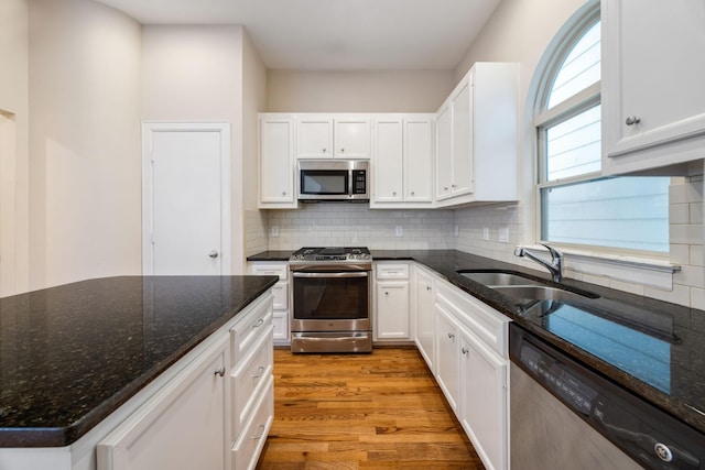 kitchen with appliances with stainless steel finishes, sink, dark stone counters, and white cabinets