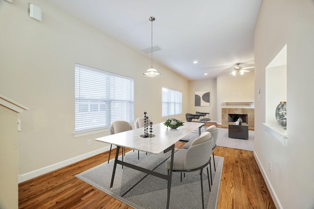 dining space with hardwood / wood-style flooring, a tile fireplace, and ceiling fan