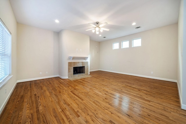 unfurnished living room with a tiled fireplace, wood-type flooring, and ceiling fan