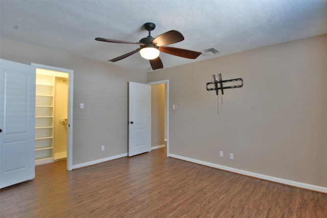 unfurnished bedroom featuring a spacious closet, a textured ceiling, a closet, ceiling fan, and dark wood-type flooring