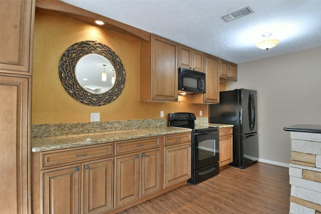 809 Pecan St, Brenham, TX 77833 - kitchen featuring black appliances, brown cabinets, wood finished floors, and light stone counters