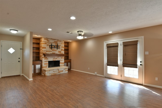 unfurnished living room with a stone fireplace, a textured ceiling, hardwood / wood-style flooring, and ceiling fan