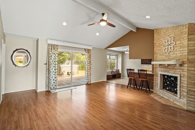 unfurnished living room featuring wood-type flooring, vaulted ceiling with beams, a large fireplace, a textured ceiling, and ceiling fan