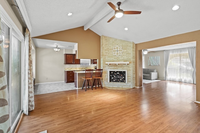 unfurnished living room featuring vaulted ceiling with beams, a large fireplace, light wood-type flooring, a textured ceiling, and ceiling fan