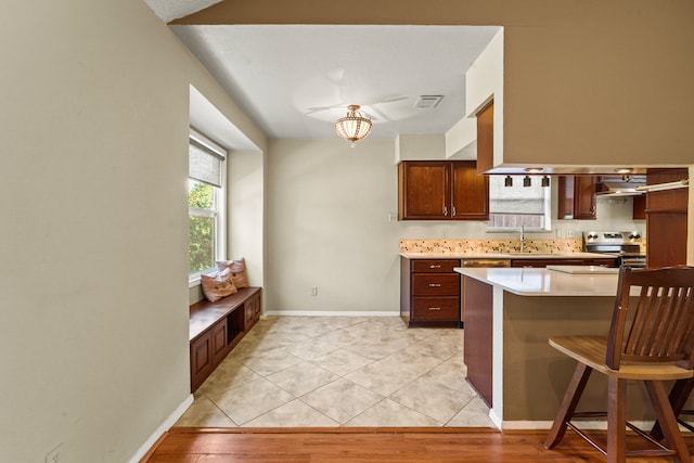 kitchen with stainless steel electric range, light tile patterned flooring, kitchen peninsula, and a kitchen bar