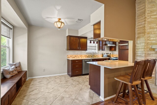 kitchen with a breakfast bar area, ventilation hood, light tile patterned flooring, and stainless steel appliances