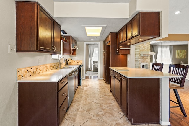 kitchen featuring a breakfast bar area, appliances with stainless steel finishes, a stone fireplace, sink, and light hardwood / wood-style floors