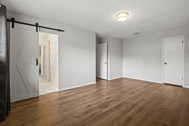 empty room featuring a textured ceiling, a barn door, and wood-type flooring