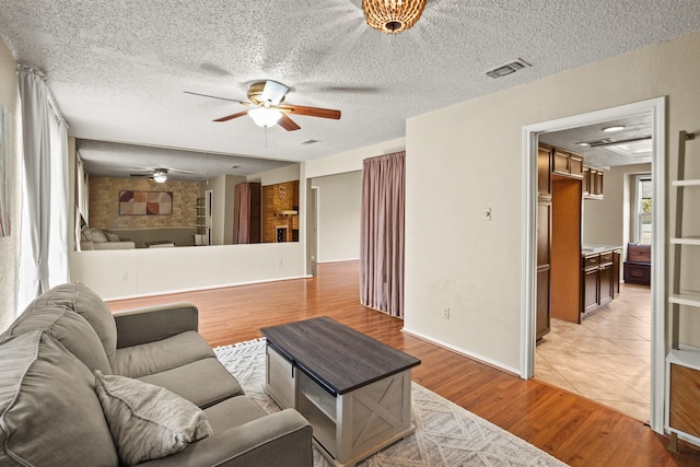 living room with a fireplace, a textured ceiling, light wood-type flooring, and ceiling fan