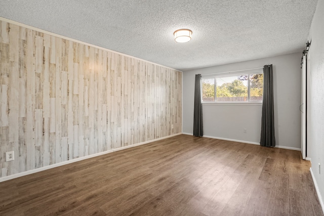 spare room featuring hardwood / wood-style flooring, a textured ceiling, wooden walls, and a barn door