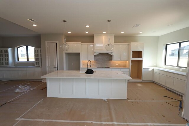 kitchen featuring pendant lighting, an island with sink, white cabinetry, and decorative backsplash