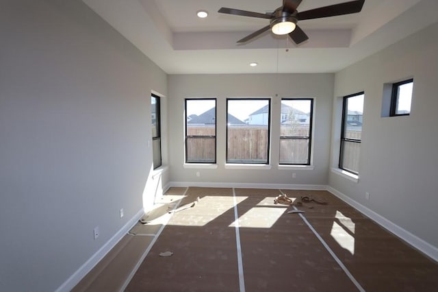 empty room with ceiling fan and a tray ceiling