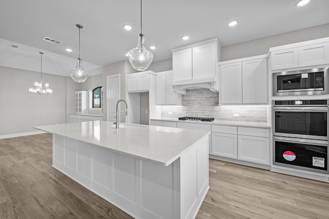 kitchen with stainless steel appliances, a kitchen island with sink, pendant lighting, and white cabinets