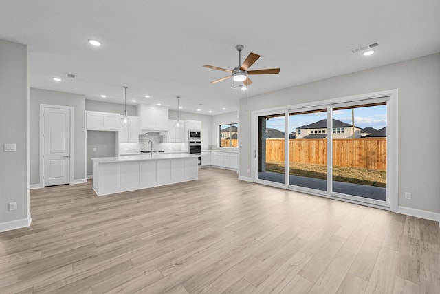 unfurnished living room with sink, ceiling fan, and light wood-type flooring