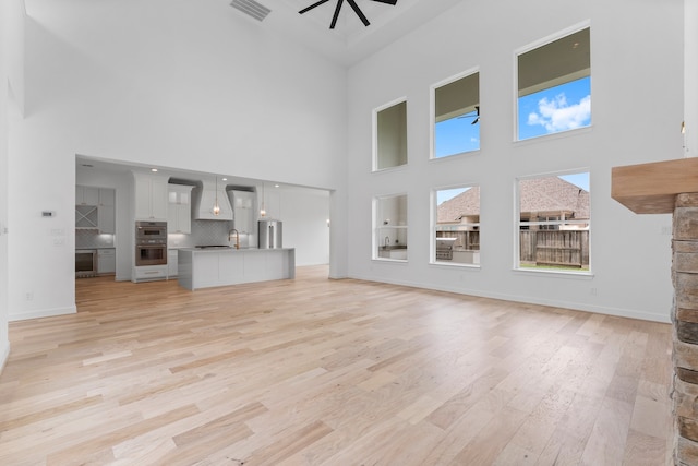 unfurnished living room featuring a towering ceiling, light hardwood / wood-style flooring, sink, and ceiling fan