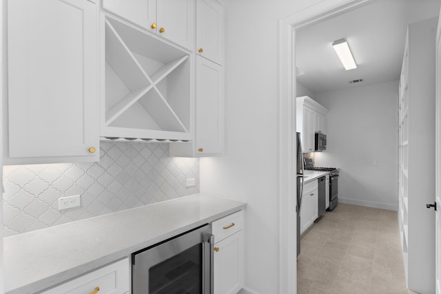 kitchen featuring wine cooler, light tile patterned floors, appliances with stainless steel finishes, backsplash, and white cabinetry