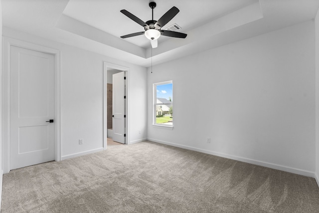 unfurnished bedroom featuring connected bathroom, light carpet, ceiling fan, and a raised ceiling