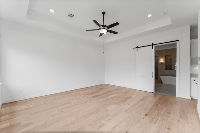 interior space with a barn door, light hardwood / wood-style flooring, a tray ceiling, and ceiling fan