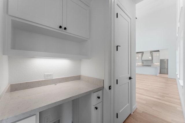 interior space with light stone countertops, light wood-type flooring, stainless steel fridge, white cabinets, and premium range hood