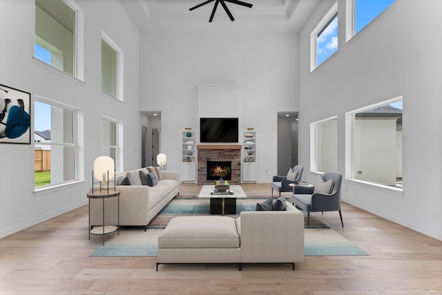 living room featuring a stone fireplace, light hardwood / wood-style flooring, a high ceiling, and ceiling fan