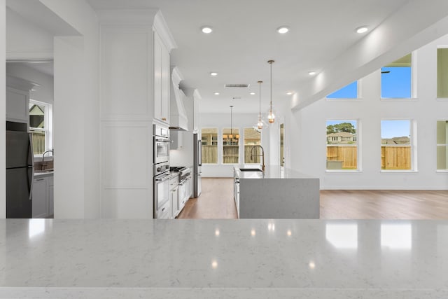 kitchen with light hardwood / wood-style flooring, stainless steel fridge, light stone counters, and pendant lighting