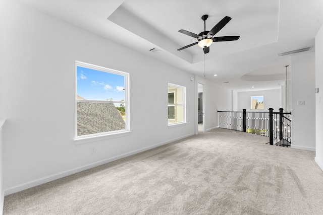 carpeted spare room featuring ceiling fan and a raised ceiling